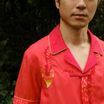 Close up of Jiannan looking directly at camera with hands behind his back, showing the right side of the shirt with embroidered dragon tail