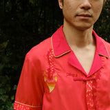 Close up of Jiannan looking directly at camera with hands behind his back, showing the right side of the shirt with embroidered dragon tail