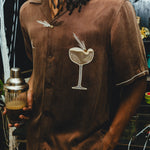 Man wearing a brown shirt with a espresso martini graphic, holding a cocktail shaker.