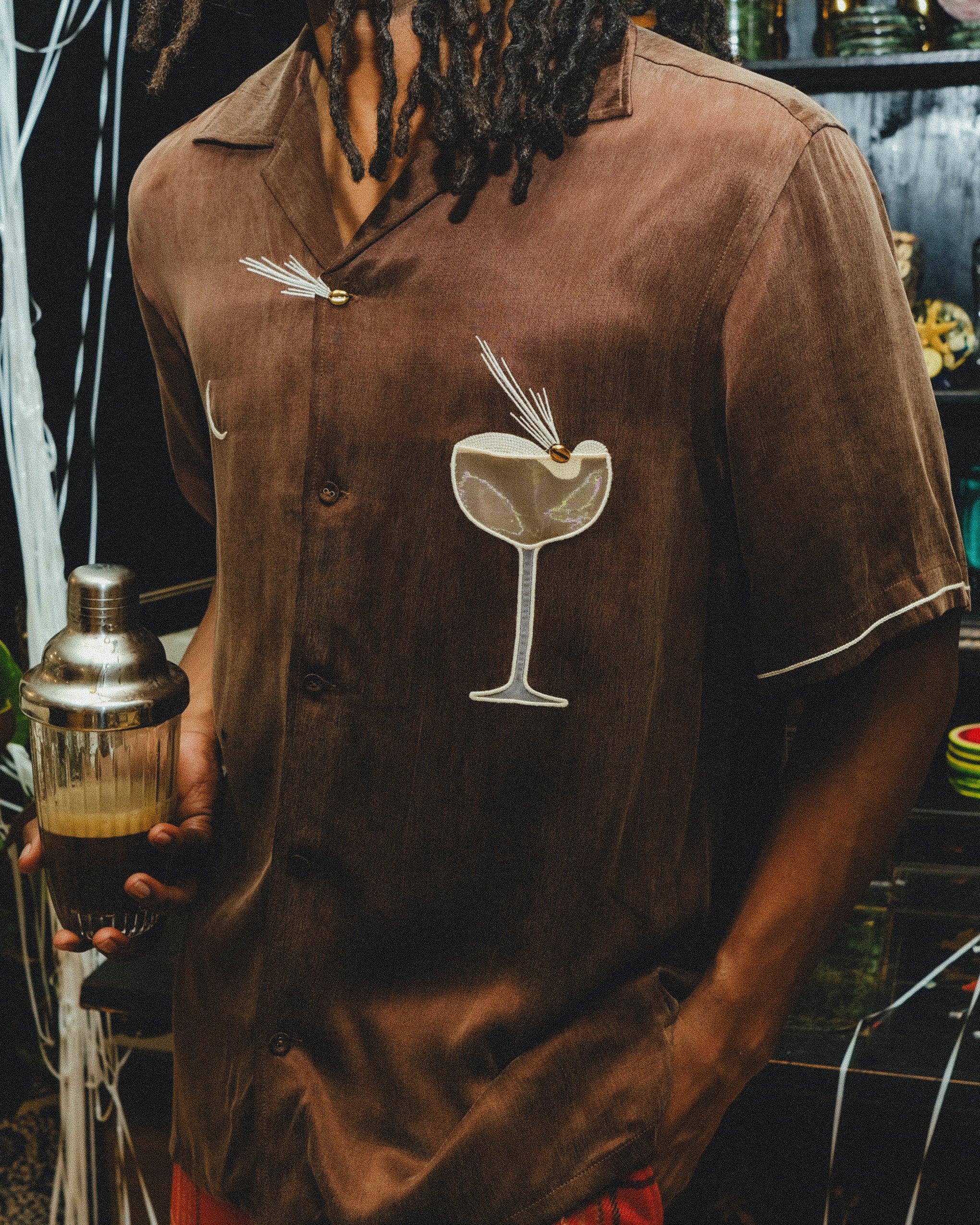 Man wearing a brown shirt with a espresso martini graphic, holding a cocktail shaker.
