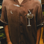 Close-up of man wearing brown espresso martini shirt, with the pocket filled with espresso beans. 