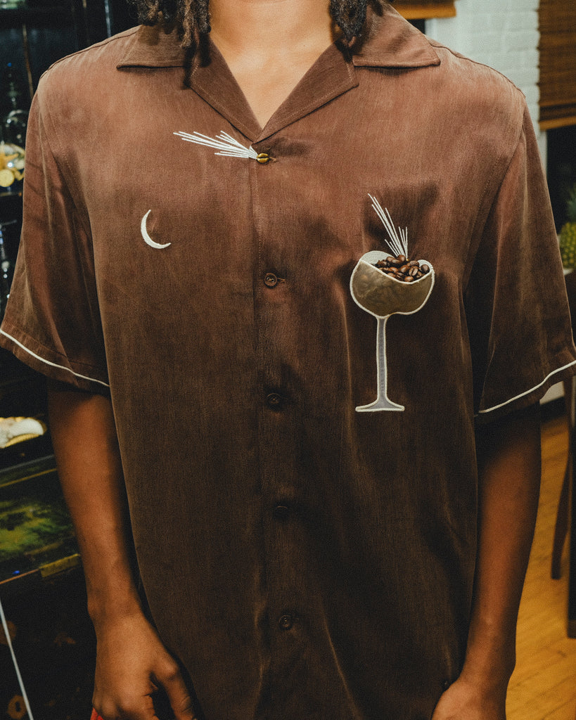 Close-up of man wearing brown espresso martini shirt, with the pocket filled with espresso beans. 