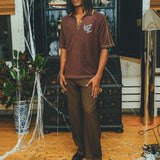 Model wearing brown SNL polo with brown pants and loafers.