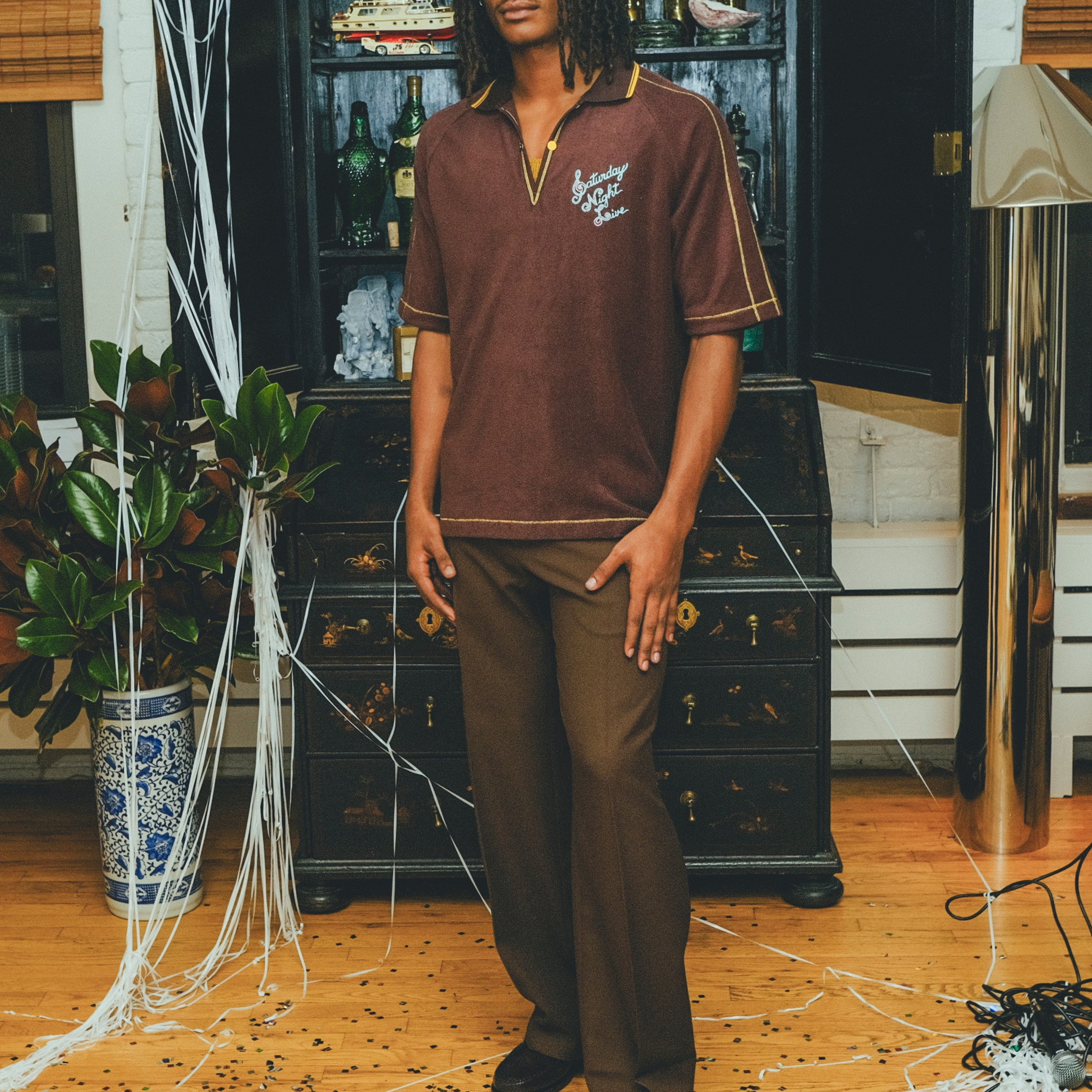Model wearing brown SNL polo with brown pants and loafers.