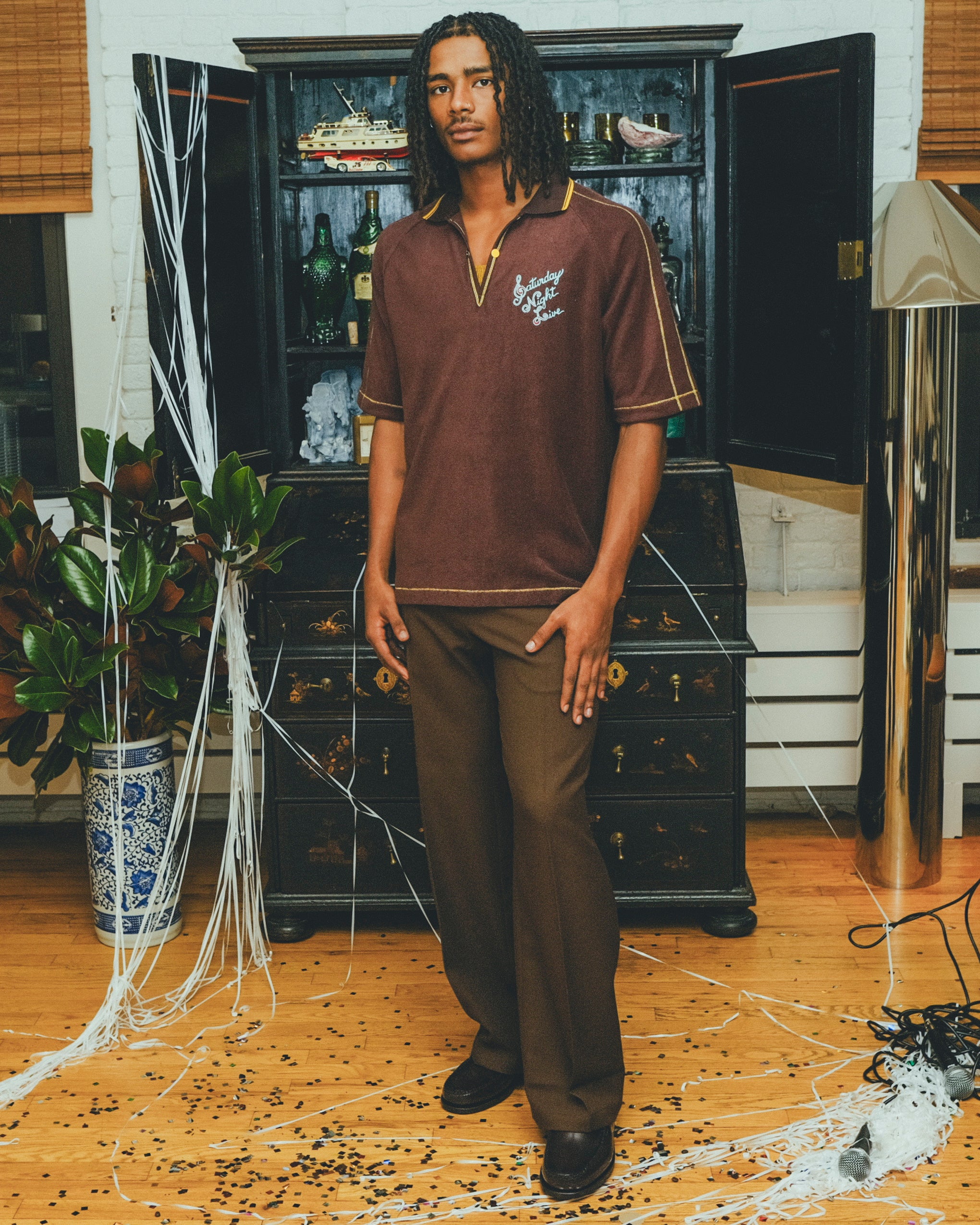 Model wearing brown SNL polo with brown pants and loafers.