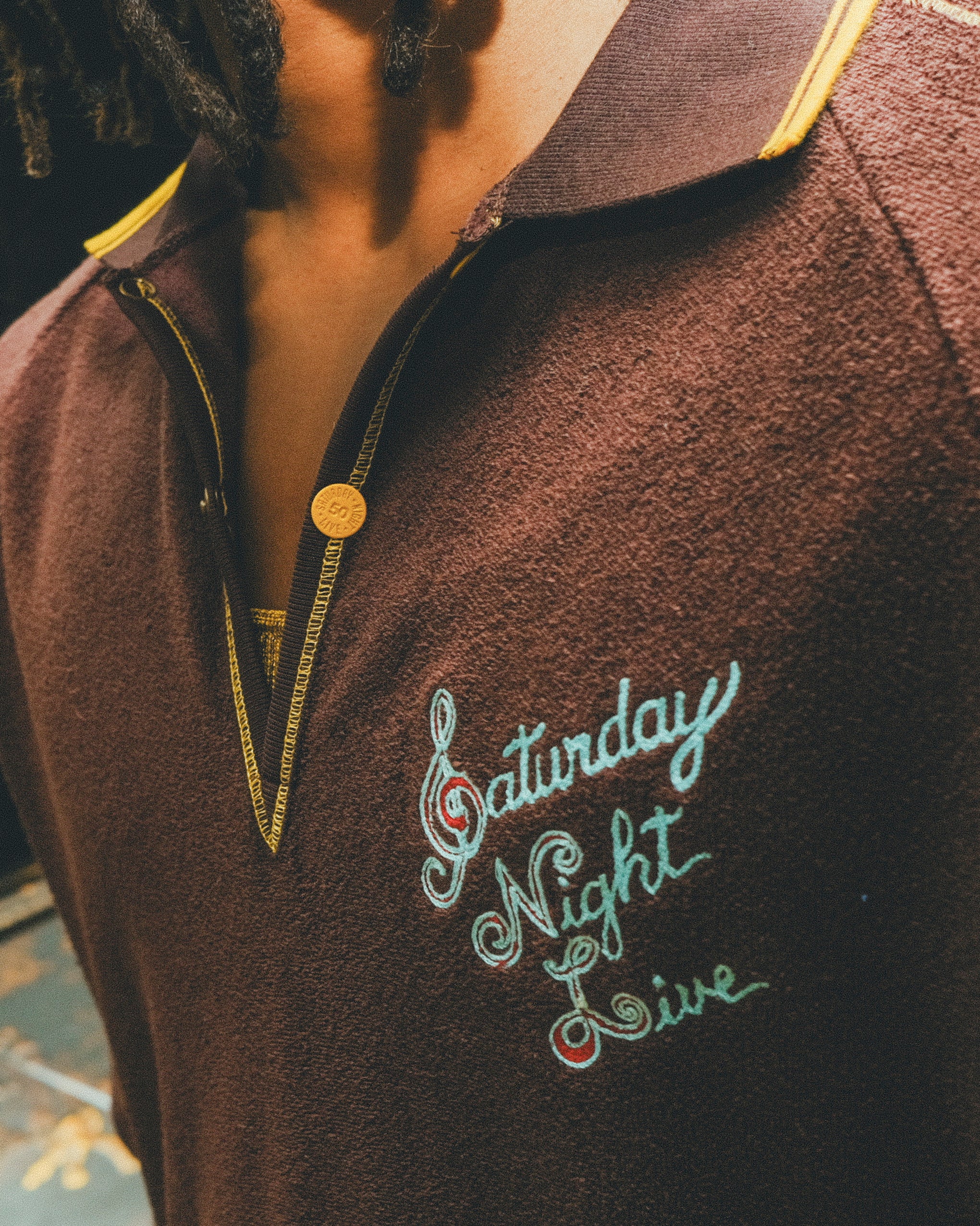 Brown terry cloth polo with 'Saturday Night Live' embroidery on the chest.