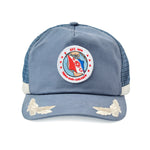 Blue hat with a circular embroidered patch on the front showing a red and blue flag over a globe. The patch reads “EST. 1904” at the top and “TERN-MARE-CAELOQUE” at the bottom, with the letters “E” and “C” on either side of a ship wheel. White embroidered wings decorate the brim.