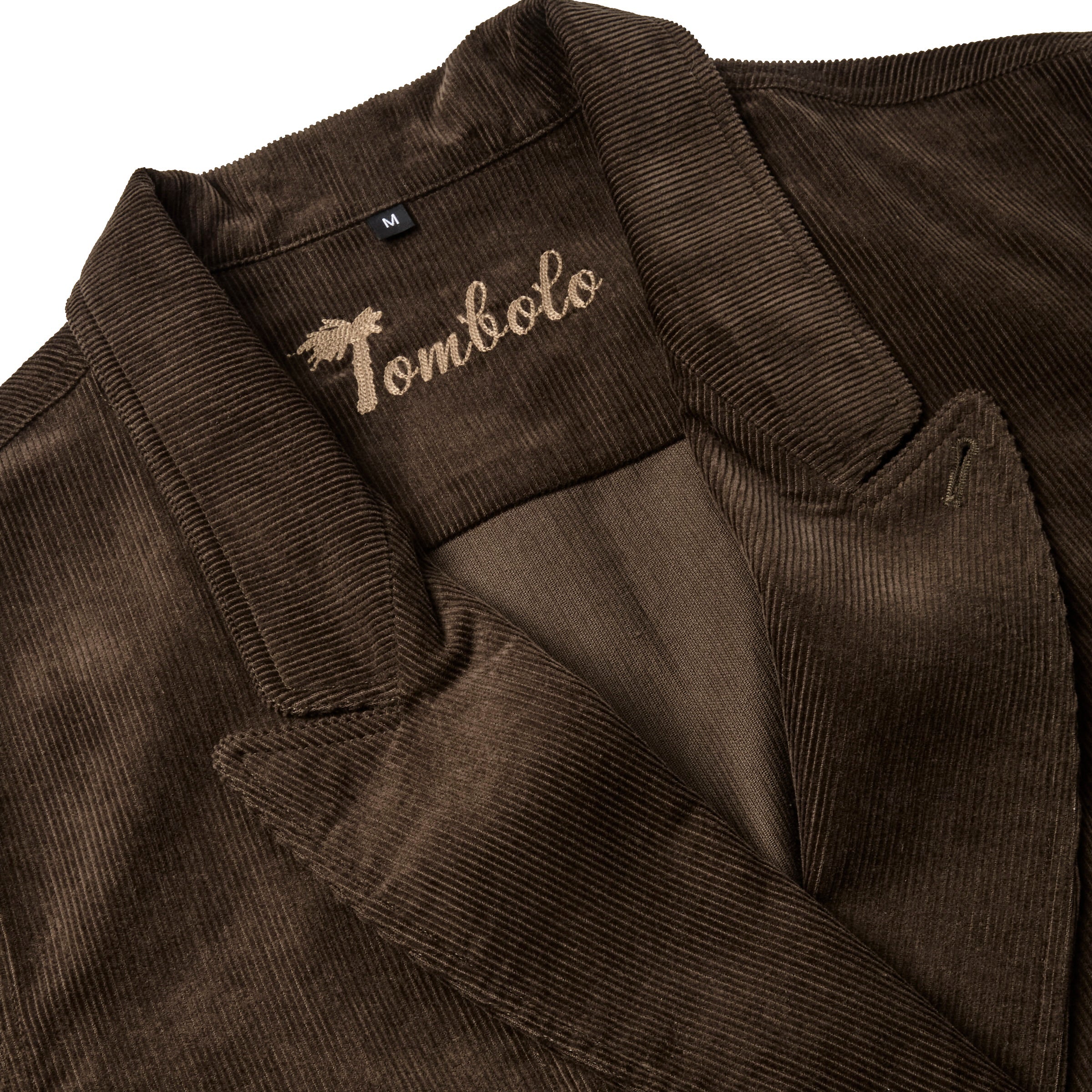 Close-up of a brown corduroy jacket with wide lapels and tan embroidered 'Tombolo' logo inside the collar.