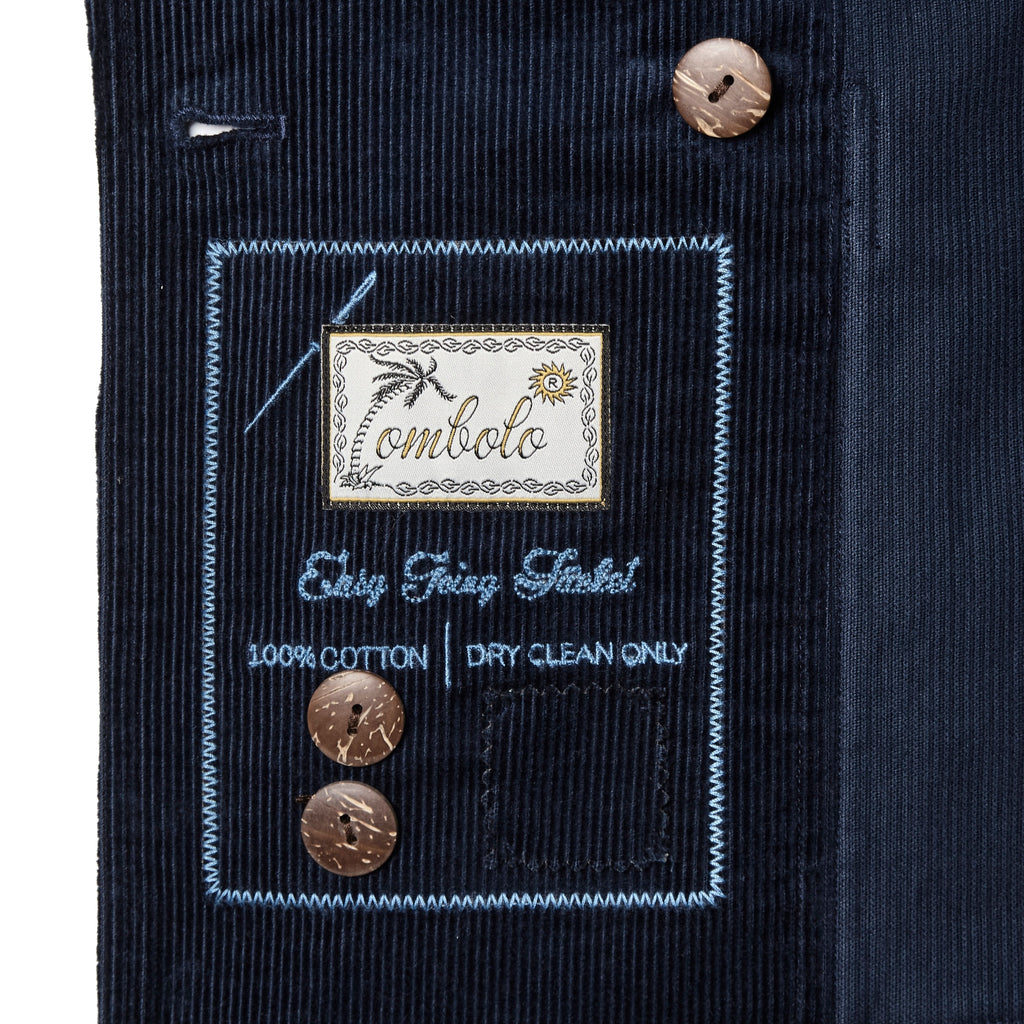 Close-up of an interior label on a navy corduroy jacket, featuring embroidered text that reads 'Tombolo' and 'Easy Going Jacket' along with care instructions and two spare buttons attached.