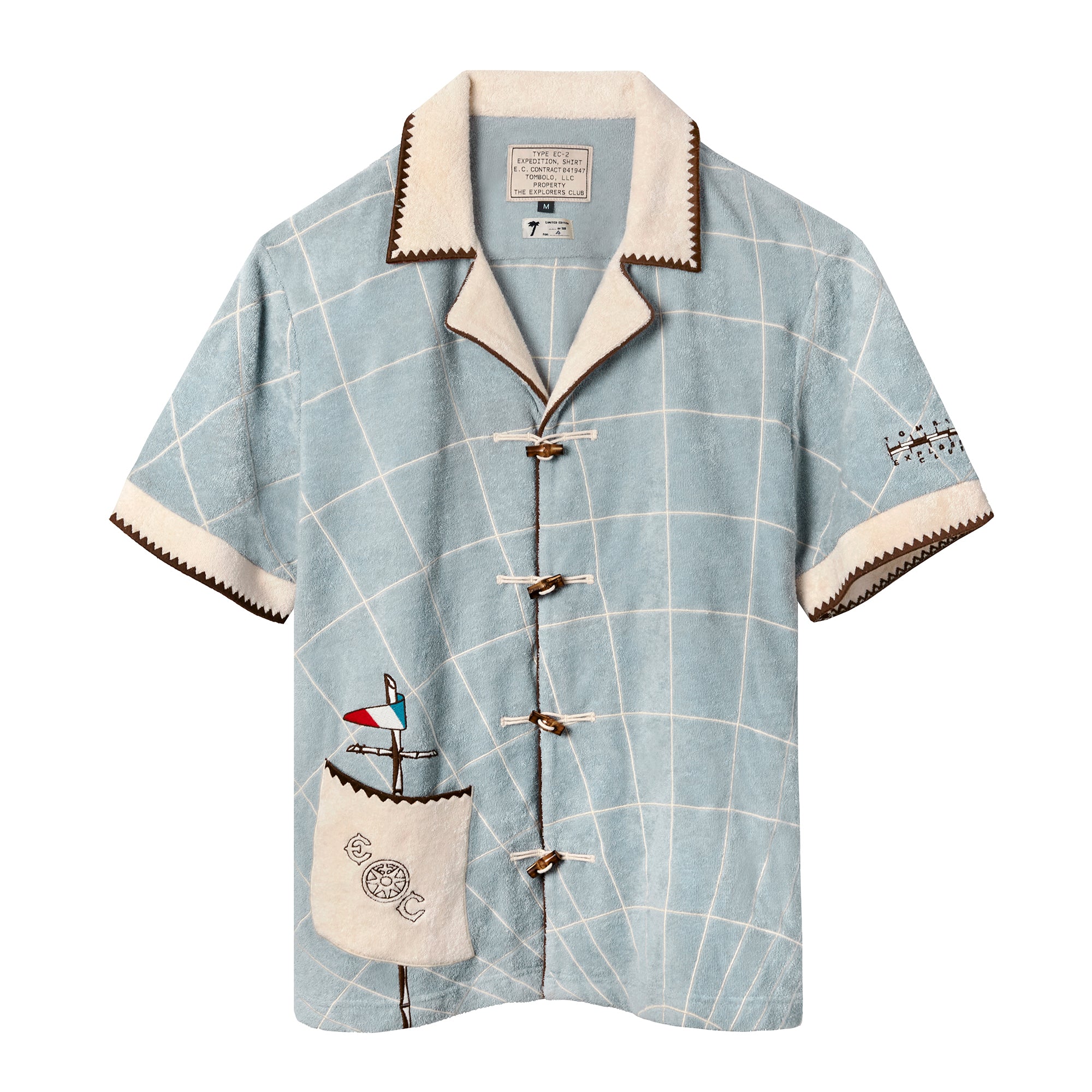 Light blue short-sleeve terry cloth shirt with an off-white grid pattern and toggle button closures down the front. The collar and sleeve cuffs feature contrast zigzag trim in brown. A front pocket is embroidered with a nautical mast, flag, and the letters “EC” on either side of a ship’s wheel. A rope ladder detail is stitched onto the right sleeve. The shirt has a vintage expedition-inspired look.
