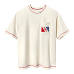 Cream-colored short-sleeve terry tee with red contrast stitching on the collar, sleeves, and hem. A chest pocket features a red and blue flag design with the letters “E” and “C” and a ship wheel emblem in the center.