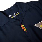 Close-up of top of garment, featuring one embroidered olive skewer, and the interior label reading "Tombolo" where the O's are embroidered olives.