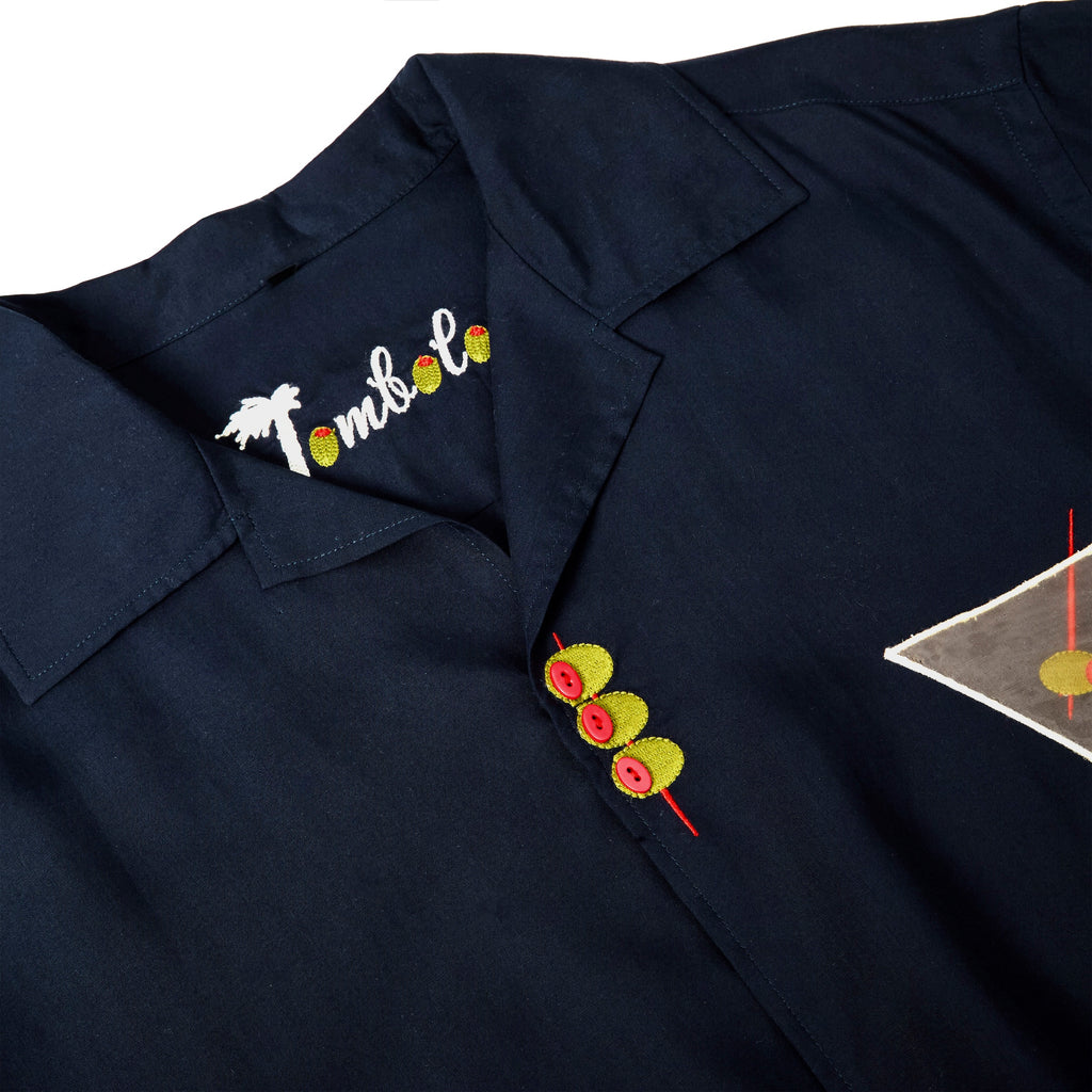 Close-up of top of garment, featuring one embroidered olive skewer, and the interior label reading "Tombolo" where the O's are embroidered olives.