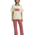 Person wearing a cream shirt with 'USA' print and red patterned pants on a white background.