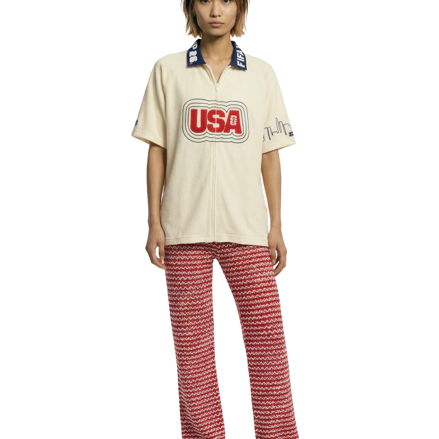 Person wearing a cream shirt with 'USA' print and red patterned pants on a white background.