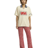 Person wearing a cream shirt with 'USA' print and red patterned pants on a white background.