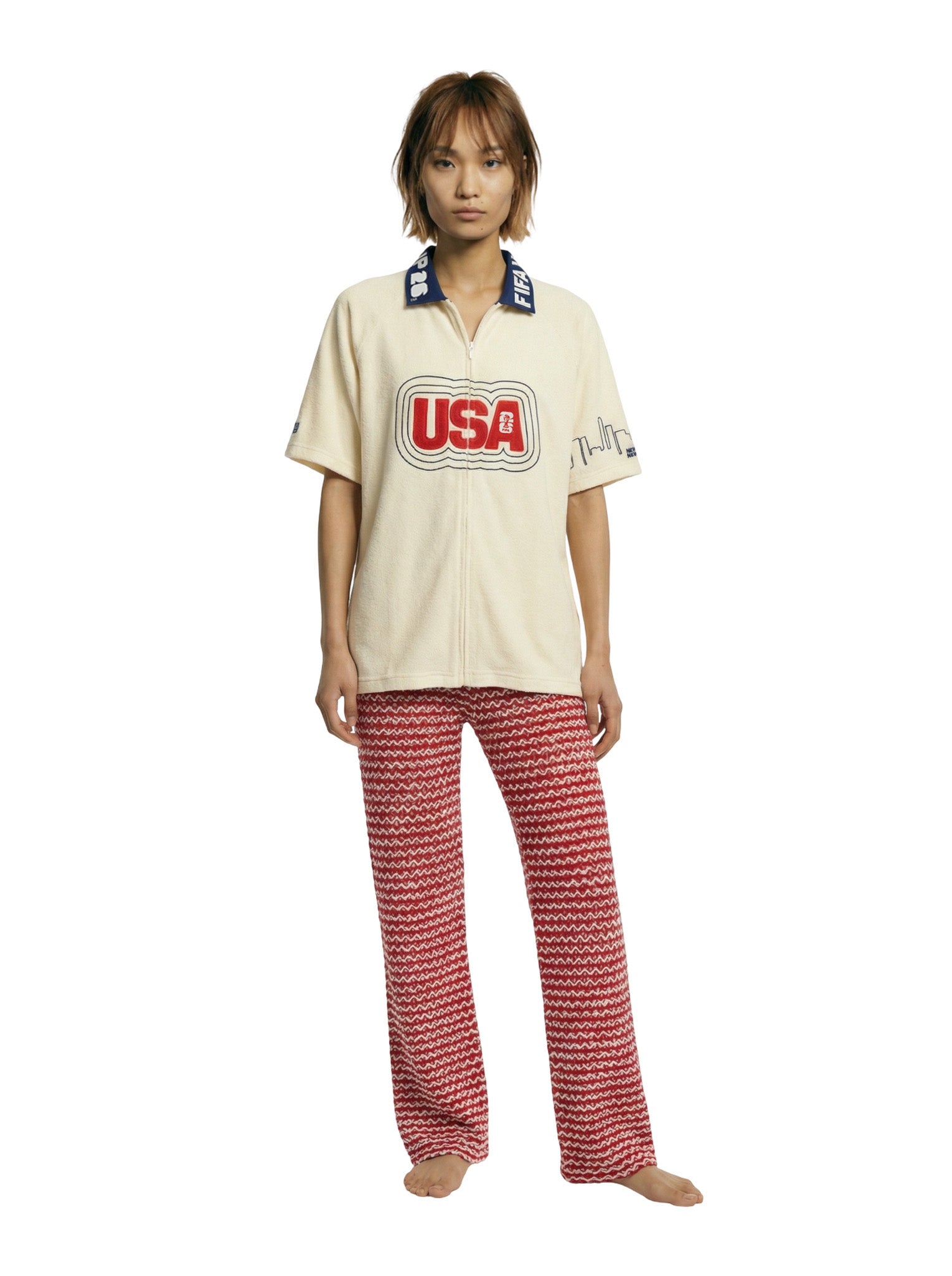 Person wearing a cream shirt with 'USA' print and red patterned pants on a white background.