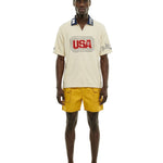 Man wearing a cream shirt with 'USA' logo and yellow shorts on a white background