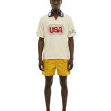 Man wearing a cream shirt with 'USA' logo and yellow shorts on a white background