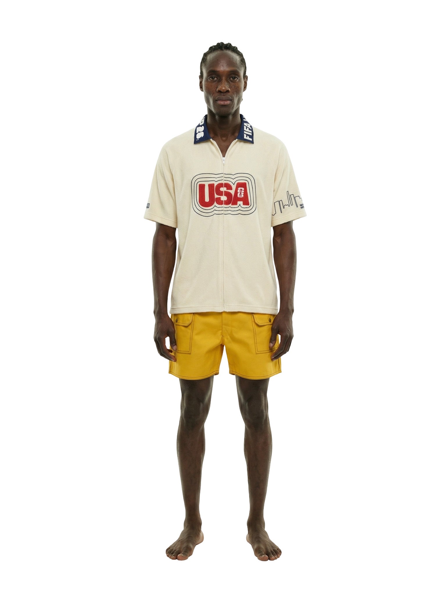 Man wearing a cream shirt with 'USA' logo and yellow shorts on a white background