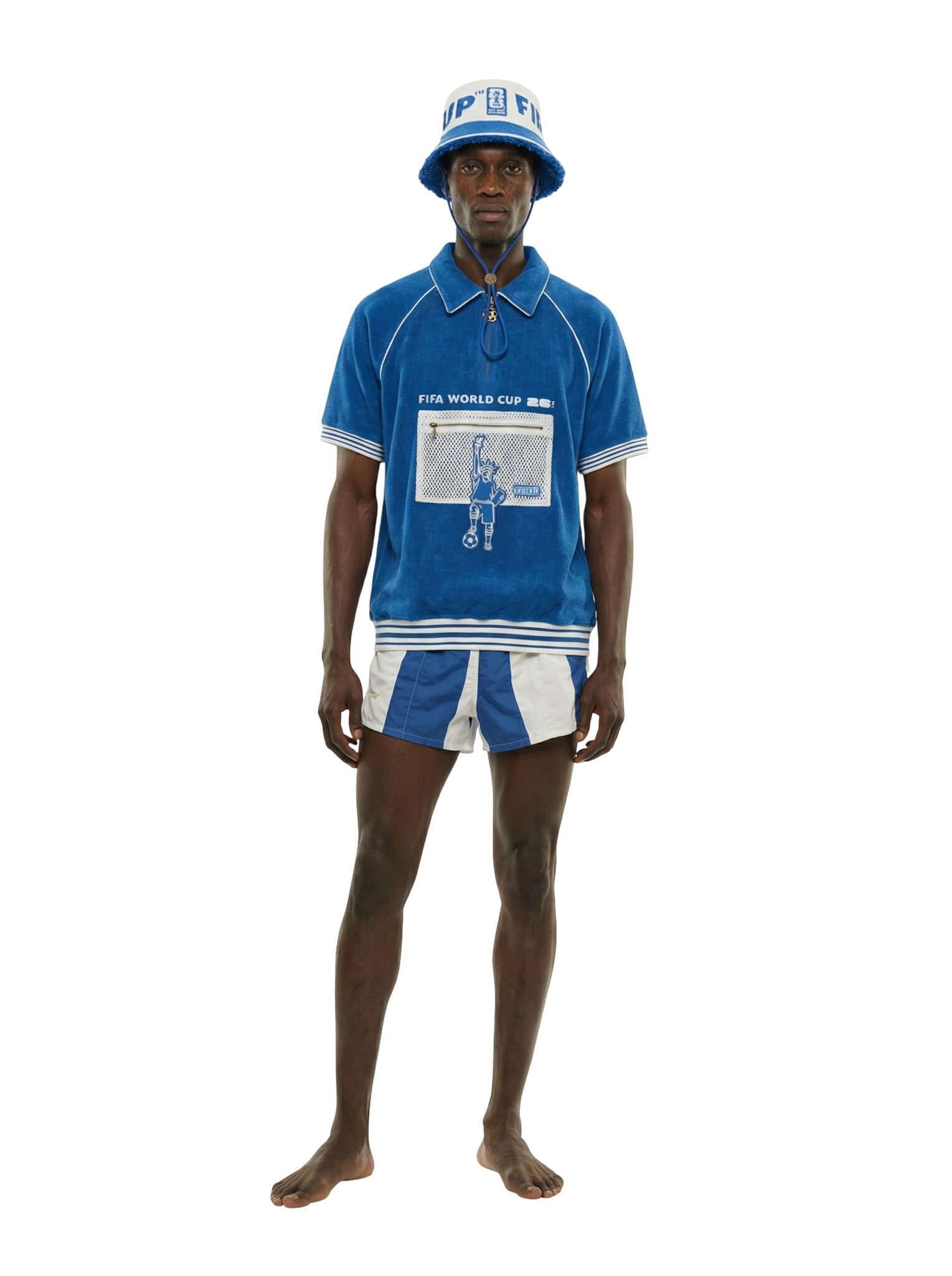 Model wearing a blue terry short-sleeve shirt with front graphic and mesh pocket detail, paired with a cream and blue FIFA World Cup bucket hat with chin cord.