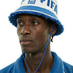 Close-up of model wearing a cream terry bucket hat with blue trim, FIFA lettering, and World Cup 2026 New York New Jersey patch, with chin cord and toggle.