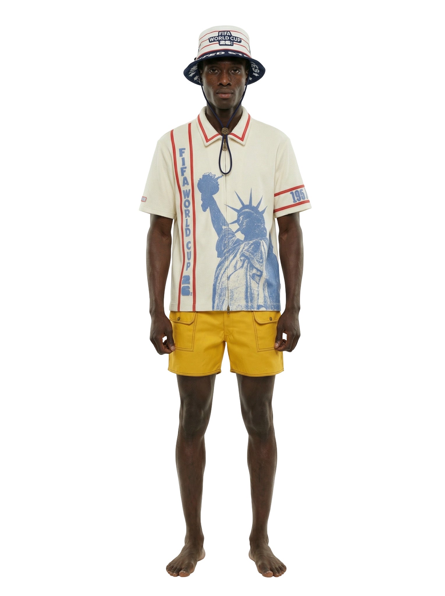 Man wearing a white shirt with a graphic design, yellow shorts, and a bucket hat on a white background