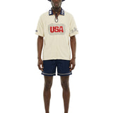 Man wearing a cream-colored shirt with 'USA' logo, navy shorts, and a matching hat on a white background