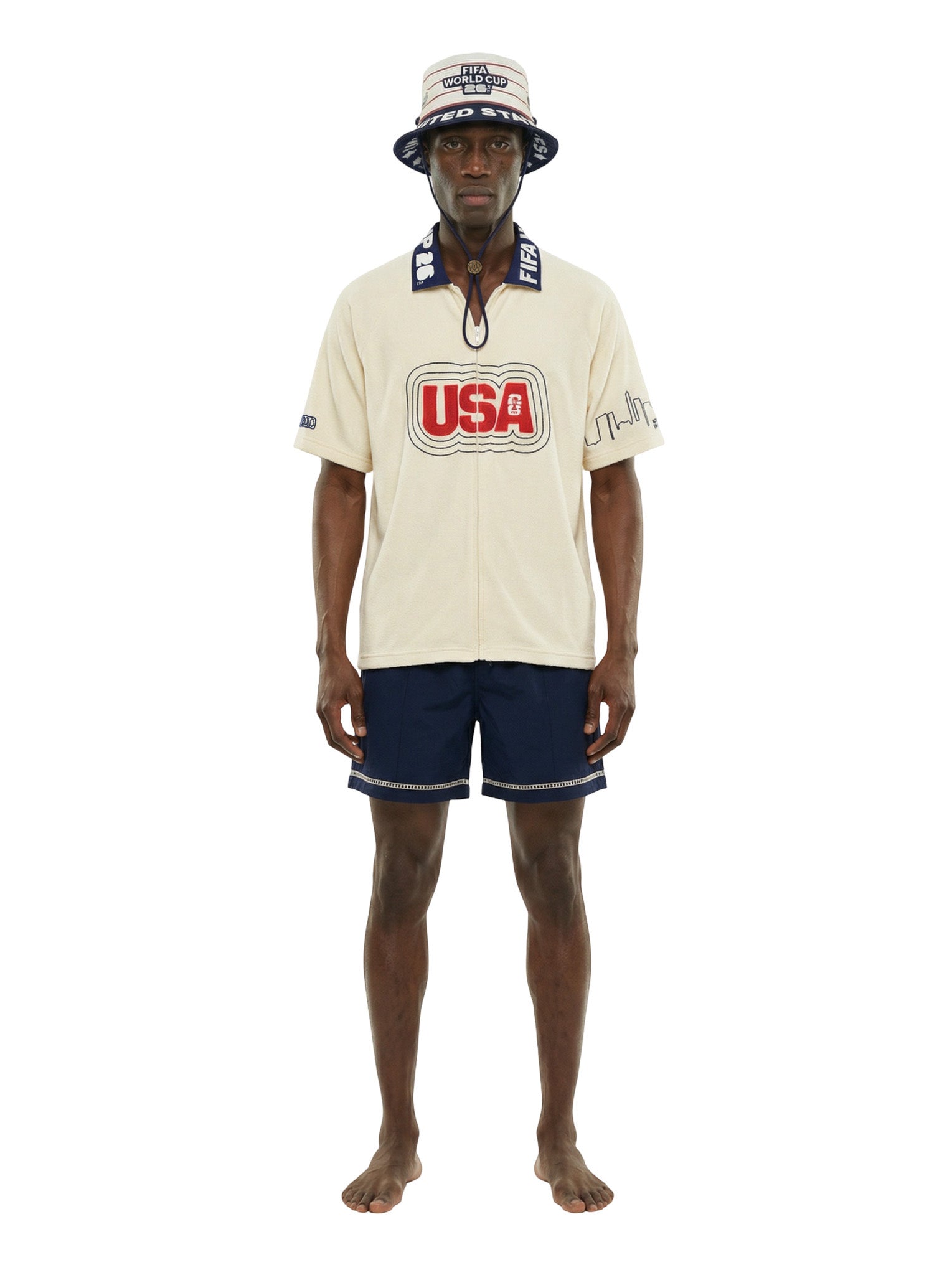 Man wearing a cream-colored shirt with 'USA' logo, navy shorts, and a matching hat on a white background