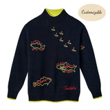 Navy knit sweater with neon yellow and red embroidered fish names, including 'Striped Bass', 'Atlantic Cod', 'Sardines', and 'Great White Shark (Human)'. Features ribbed cuffs and hem with yellow contrast detail, and red embroidered 'Tombolo' text at the waist.