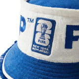 Close-up of cream and blue terry bucket hat showing FIFA World Cup 2026 New York New Jersey patch and blue brim with textured fringe edge.