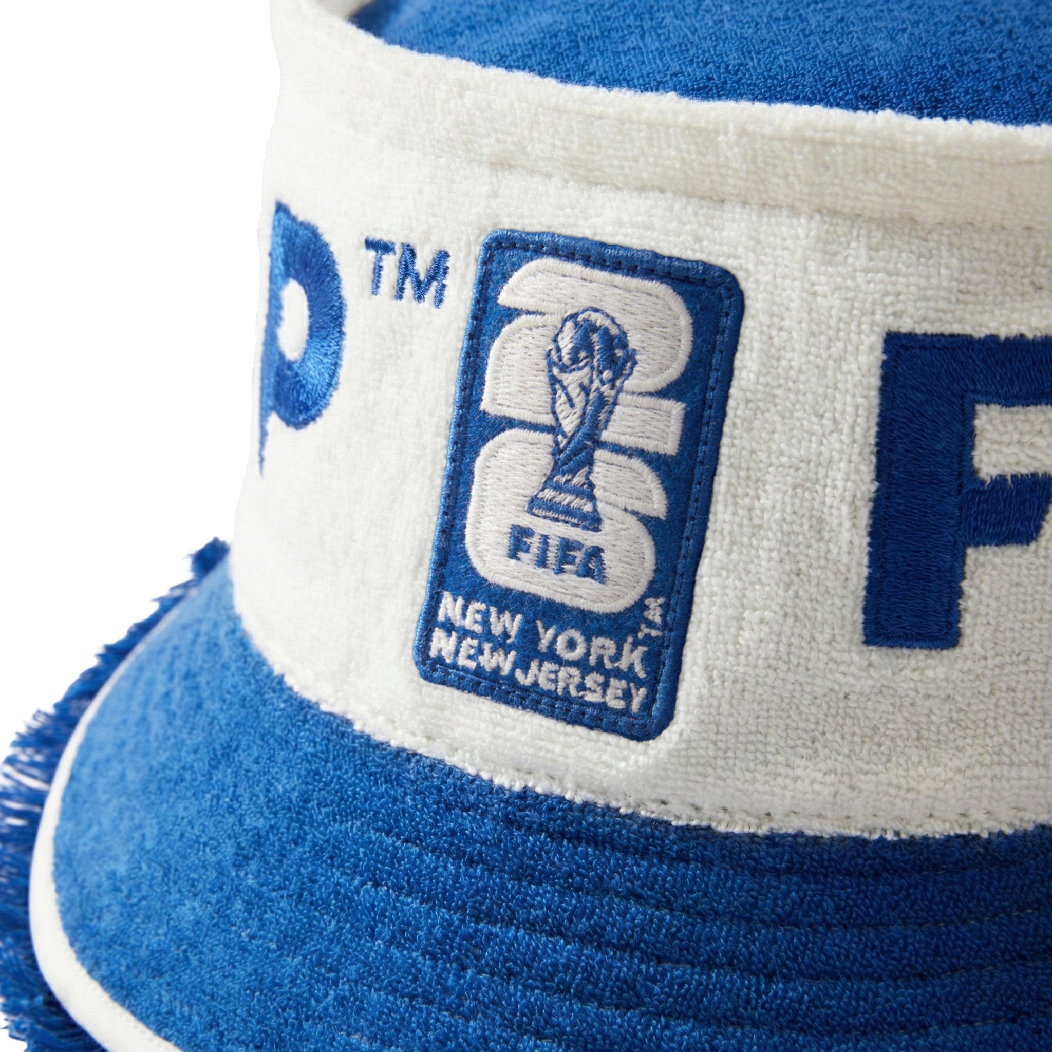 Close-up of cream and blue terry bucket hat showing FIFA World Cup 2026 New York New Jersey patch and blue brim with textured fringe edge.