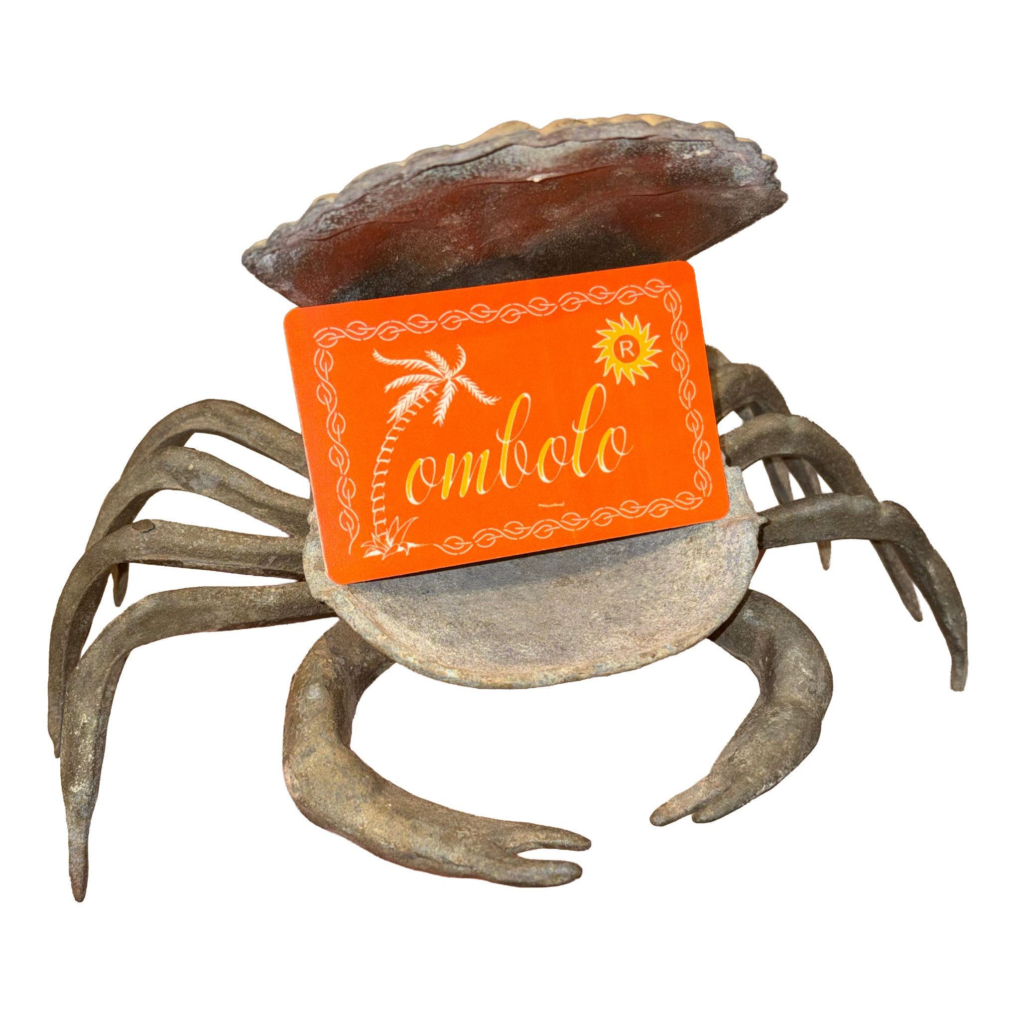 Orange Tombolo gift card with decorative leaf border held in a rusty metal crab-shaped ashtray