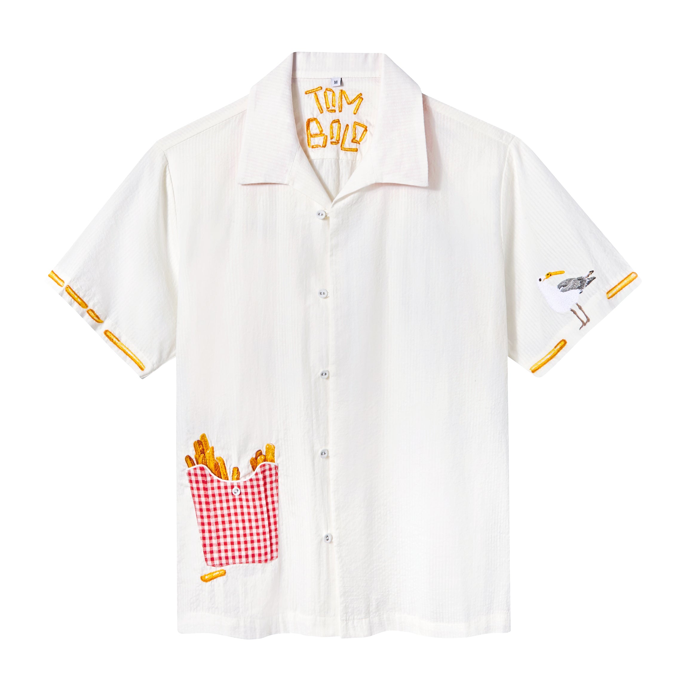 White short-sleeve button-down shirt features a red gingham pocket filled with embroidered French fries, a seagull on the right sleeve, and 'Tombolo' spelled in fries under the collar.
