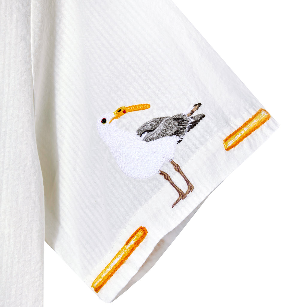Close-up of a white shirt sleeve featuring an embroidered seagull holding a French fry in its beak, with additional embroidered fries decorating the hem.