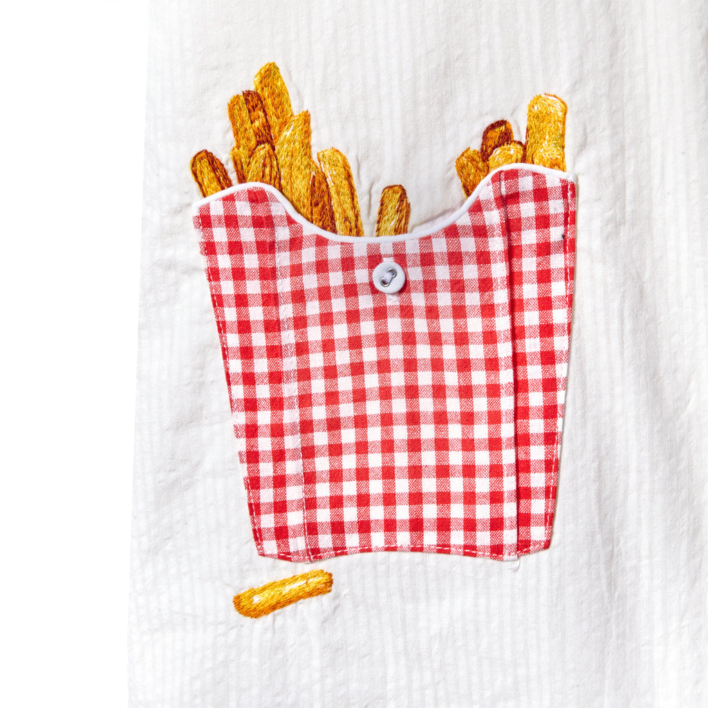 Close-up of a red gingham pocket on a white shirt, with embroidered French fries appearing to spill out.