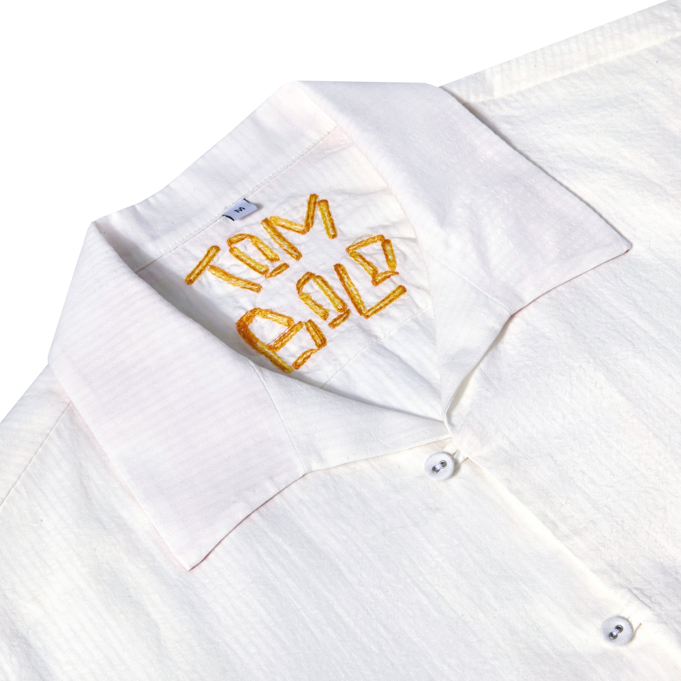 Close-up of the inside collar of a white button-down shirt with the word 'Tombolo' embroidered in golden French fries.