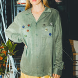 Woman wearing a green SNL shirt and sunglasses in front of a bar cabinet. 