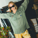 Woman wearing a green SNL shirt with colorful buttons and yellow shorts.