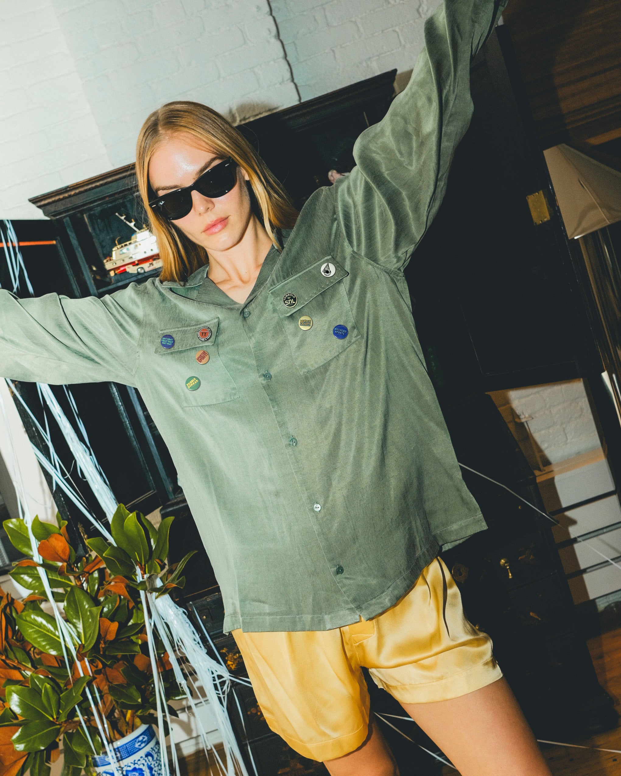 Woman wearing a green SNL shirt with colorful buttons and yellow shorts.