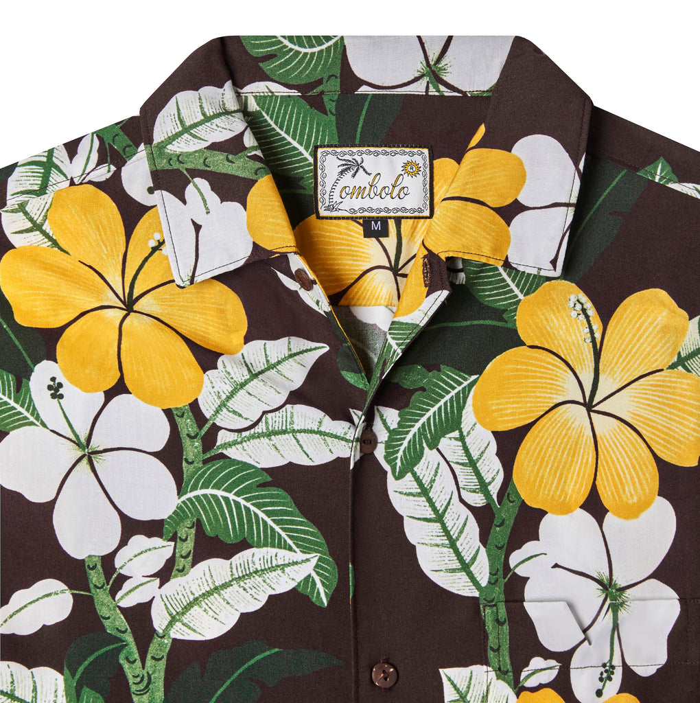 Close up front-facing product image of "Night Bloom" buttoned shirt with one button undone that emphasizes intricacies of hibiscus floral pattern that features yellow, green, and white accents on a brown base, in addition to the tag which shows a leaning palm tree as the "T" in Tombolo in a script font.