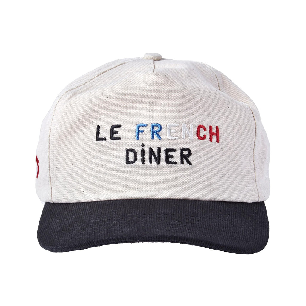 A beige canvas baseball cap with a black brim. The front is embroidered with the words “LE FRENCH DÎNER.” The word “FRENCH” is stitched in blue, white, and red letters, while the other text is in black.
