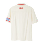 Back of beige short-sleeve cabana shirt with red collar piping, FIFA World Cup 26 logo below collar, and 2026 armband detail on wearer’s left sleeve.