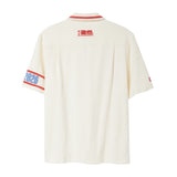 Back of beige short-sleeve cabana shirt with red collar piping, FIFA World Cup 26 logo below collar, and 2026 armband detail on wearer’s left sleeve.