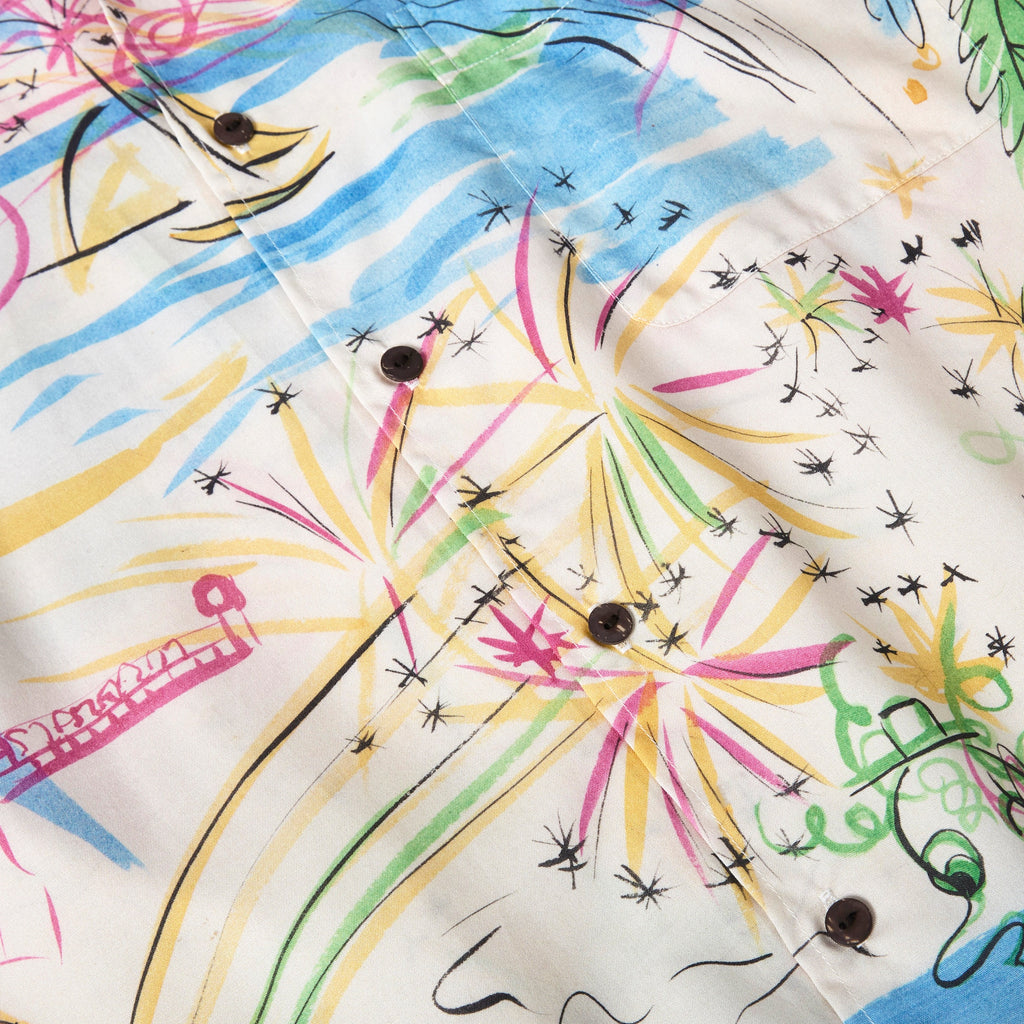 Close-up of a cream-colored button-down shirt featuring an abstract print with fireworks, waves, and sketch-style figures in yellow, pink, blue, and green. 