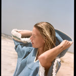 woman closes eyes on the beach pulling up hood of poncho