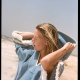woman closes eyes on the beach pulling up hood of poncho
