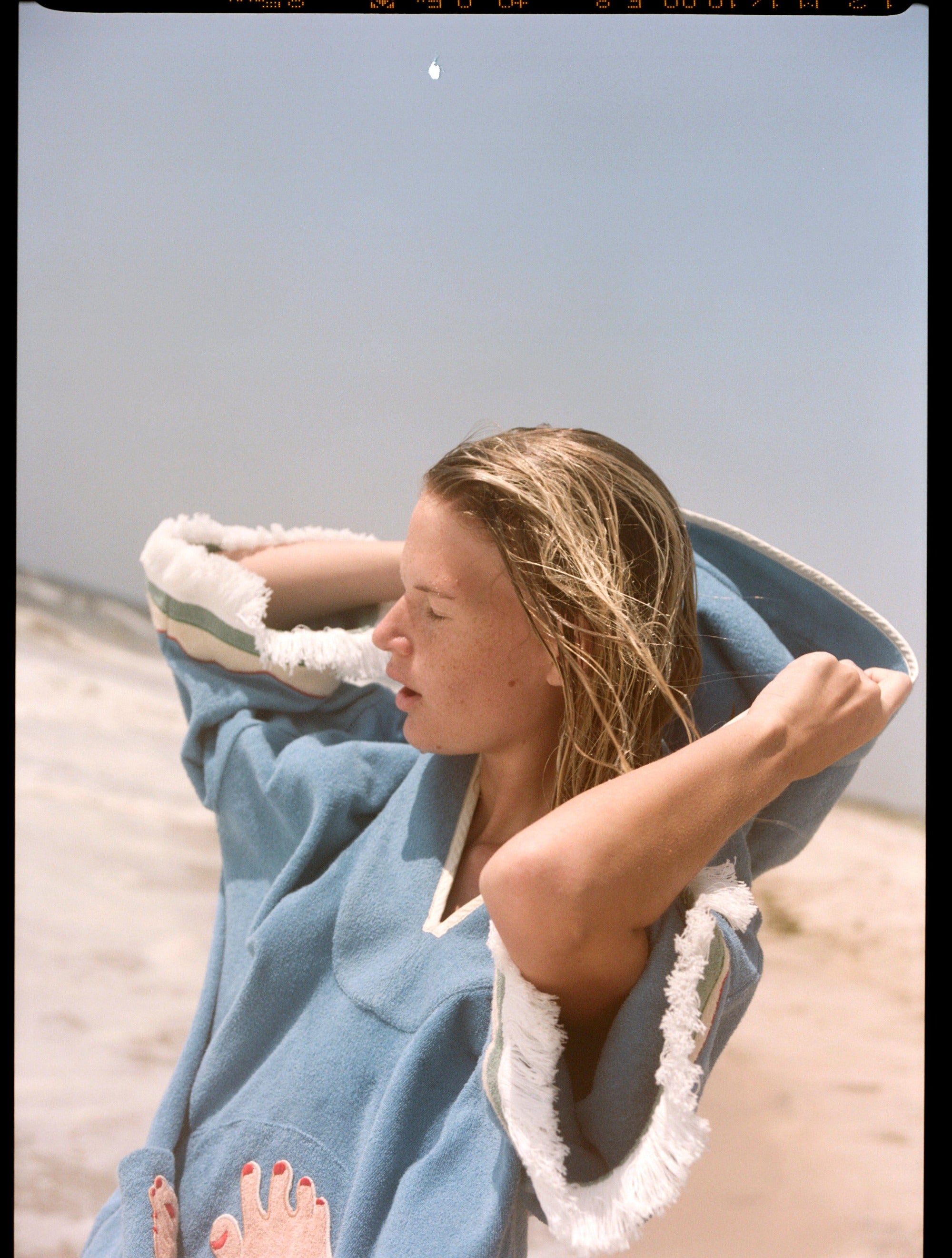 woman closes eyes on the beach pulling up hood of poncho