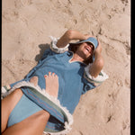 woman laughs lying down on sand with hood pulled over eyes