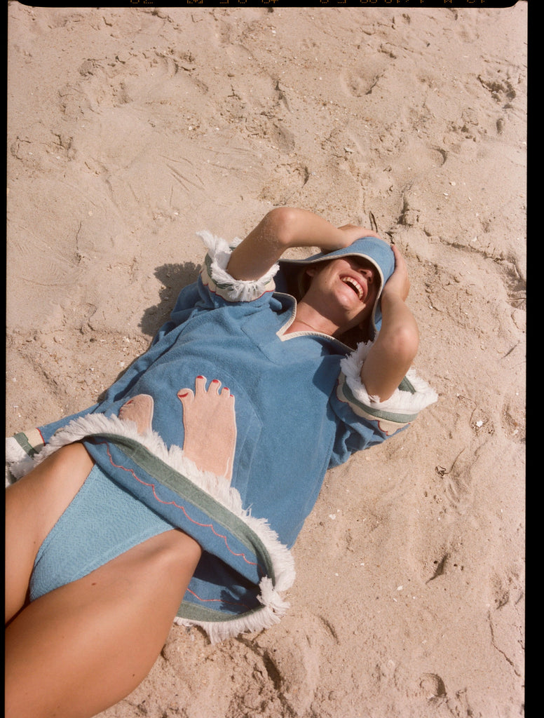 woman laughs lying down on sand with hood pulled over eyes